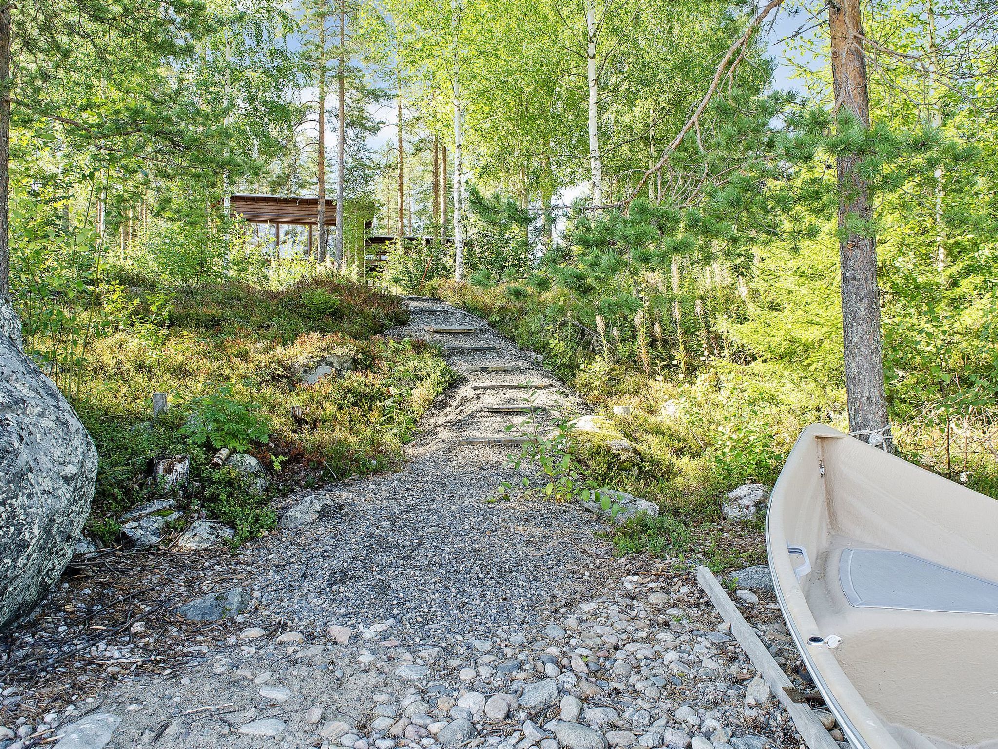 Un chemin de gravier mène à un chalet en bois situé dans une zone boisée.