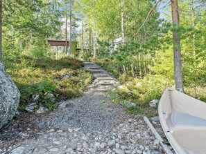 Un sendero de grava conduce a una cabaña de madera en un área boscosa.