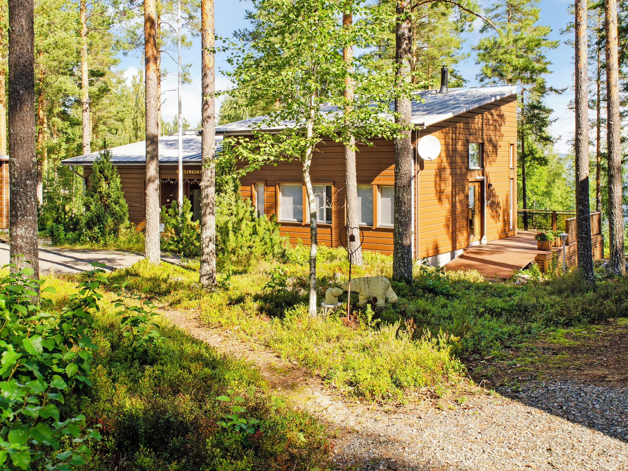 En stuga med en veranda, omgiven av träd och en grusgång.