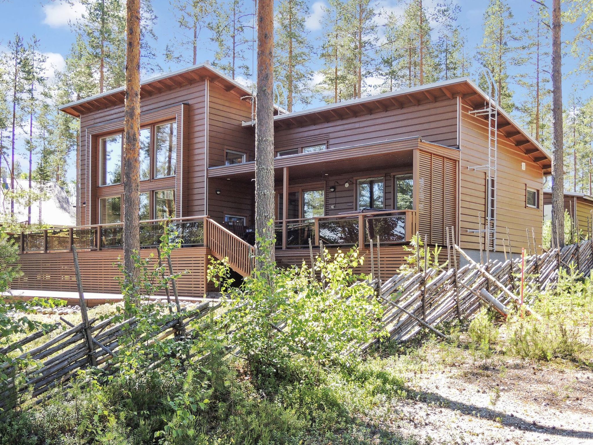 A two-story wooden cabin with a balcony, surrounded by trees and vegetation.