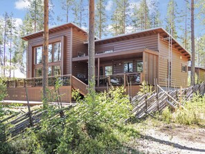 Une cabane en bois à deux étages, dotée d’un balcon et entourée d’arbres et de végétation.