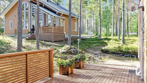 A wooden deck with a wooden fence, a small wooden structure with a porch, and a house with a sloped roof surrounded by trees. - Pielislinna/loma-koli by Interhome (Lieksa)