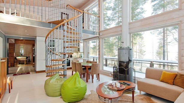 A spacious living area with a wooden staircase, a fireplace, and large windows offering a view of the forest. - Pielislinna/loma-koli by Interhome (Lieksa)