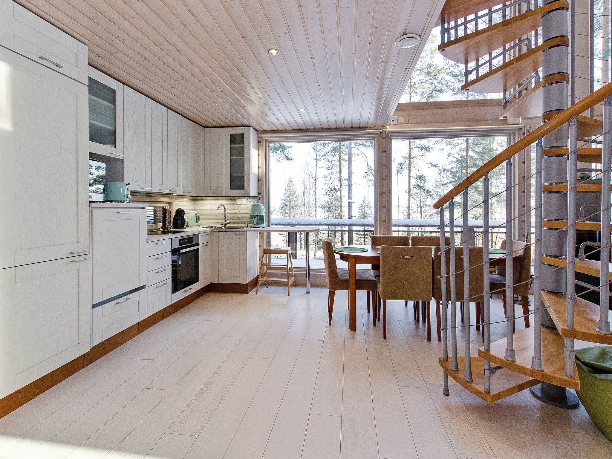 A modern kitchen with white cabinets, a dining area with a wooden table and chairs, and a spiral staircase.