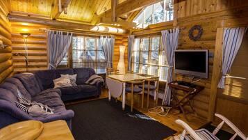 Ein gemütliches Blockhaus-Interieur mit einer Couch, einem Esstisch, einem Fernseher und einem Kamin.