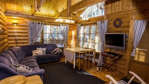 Interior de una cabaña de madera con sofá, mesa, televisor y paredes de madera.