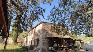 Un edificio in pietra con un portico coperto, sedute all'aperto e un muro di pietra sullo sfondo.