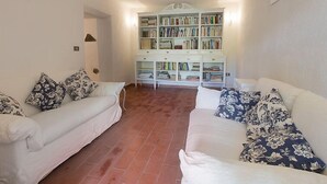Un soggiorno con due divani bianchi, una libreria e un pavimento piastrellato.
