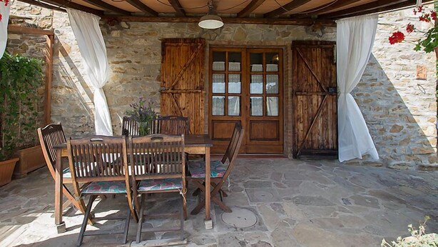 Un patio in pietra con tavolo e sedie di legno, una rustica porta in legno e un muro in pietra.