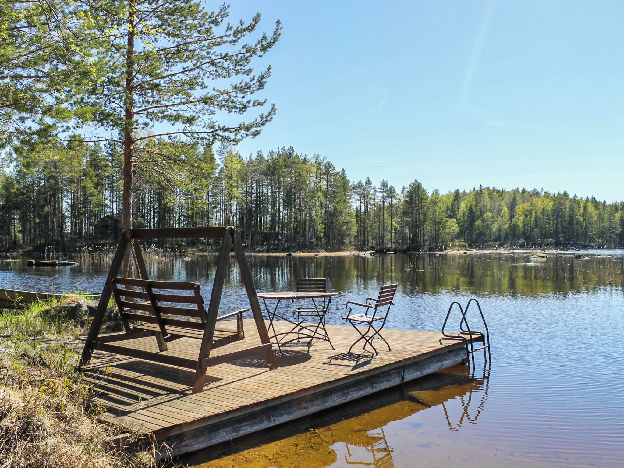 Un muelle de madera con un banco y una mesa, con vistas a un lago tranquilo rodeado de árboles.