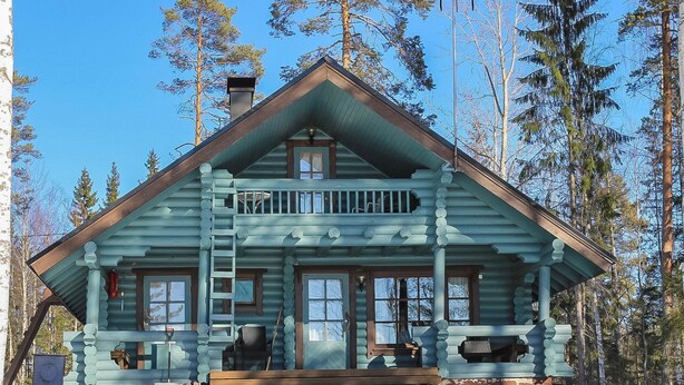 A log cabin with a balcony, large windows, and a chimney.