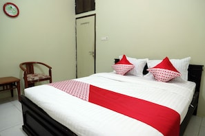 A neatly made bed with a white and red bedspread, two pillows with a red and white pattern, a wooden chair, and a door with a light switch above it.