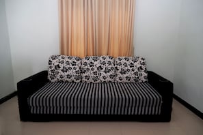 A sofa with floral and striped upholstery in a room with a plain wall and a curtain.