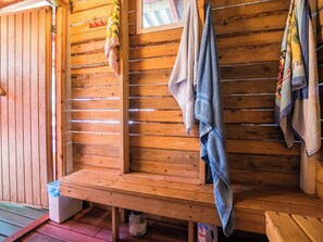 A wooden bench with towels hanging on a rack, a wooden wall, and a small trash bin.