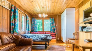 L’intérieur d’un chalet accueillant, avec un plafond en bois, un canapé en cuir, une table à manger et un téléviseur posé sur une étagère.