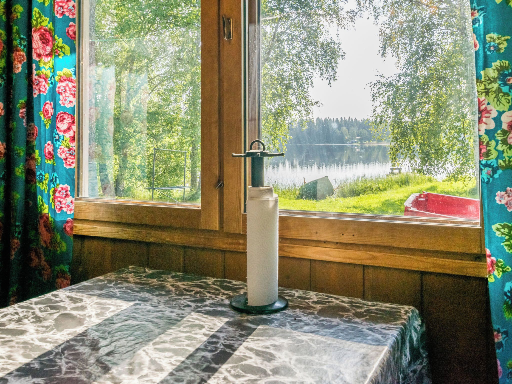 Huone, jossa on ikkuna, josta avautuu näkymä järvelle, pöydällä palaa kynttilä ja ikkunoissa on kukalliset verhot.