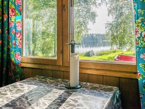 Una habitación con ventana que da a un lago, una vela sobre una mesa y cortinas con motivos florales.