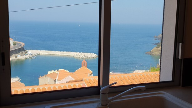 A view from a window overlooking a coastal area with a sea, a breakwater, and buildings with orange-tiled roofs. - Village house, sea view, Cerbère (Cerbère)
