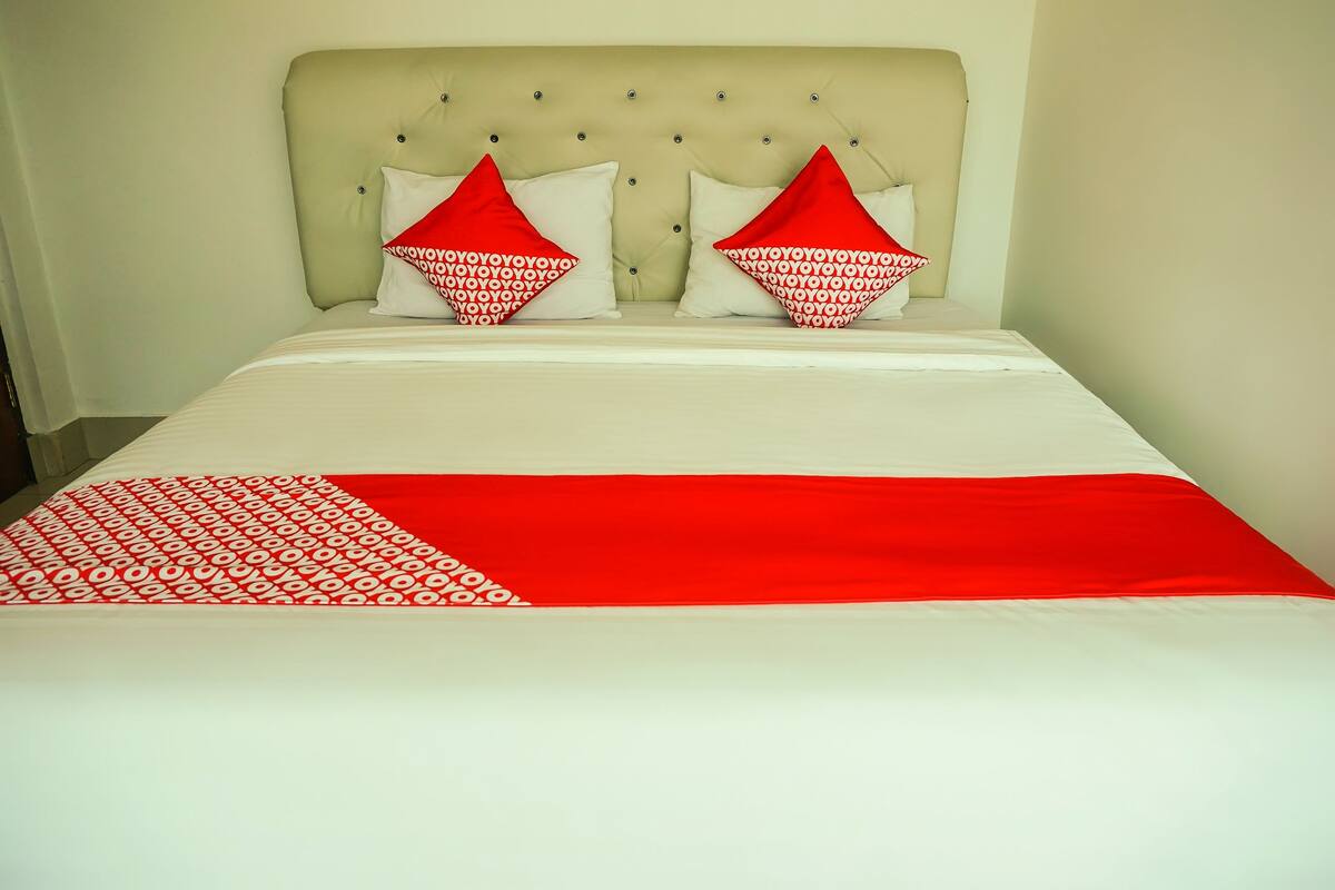 Un lit avec une couvre-lit blanche et rouge, deux oreillers rouges et blancs, et une tête de lit capitonnée.