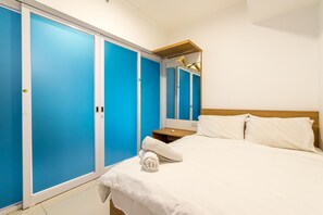 A hotel room with a bed, white linens, a wooden nightstand, a white towel, and blue sliding doors. - JK Maritime Luxury Suite (George Town)