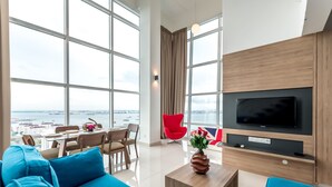 Ein modernes Wohnzimmer mit großem Fernseher, blauem Sofa und einem Essbereich mit einem roten Sessel.