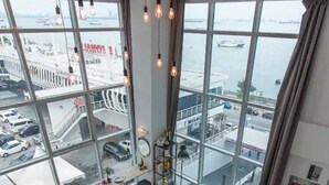 Ein Hotelzimmer in einem Hochhaus mit großem Fenster und Blick auf eine belebte Straße sowie ein Gewässer.