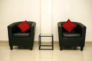 Two comfortable armchairs sit on a tiled floor, each with a cushion, accompanied by a small side table.