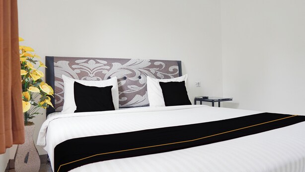 A neatly made bed with a black and white bedspread, a decorative headboard, and a vase of yellow flowers on the side.