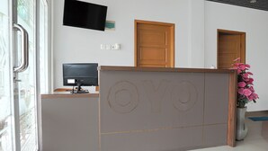 A reception desk with a monitor, a wooden door, and a potted plant.