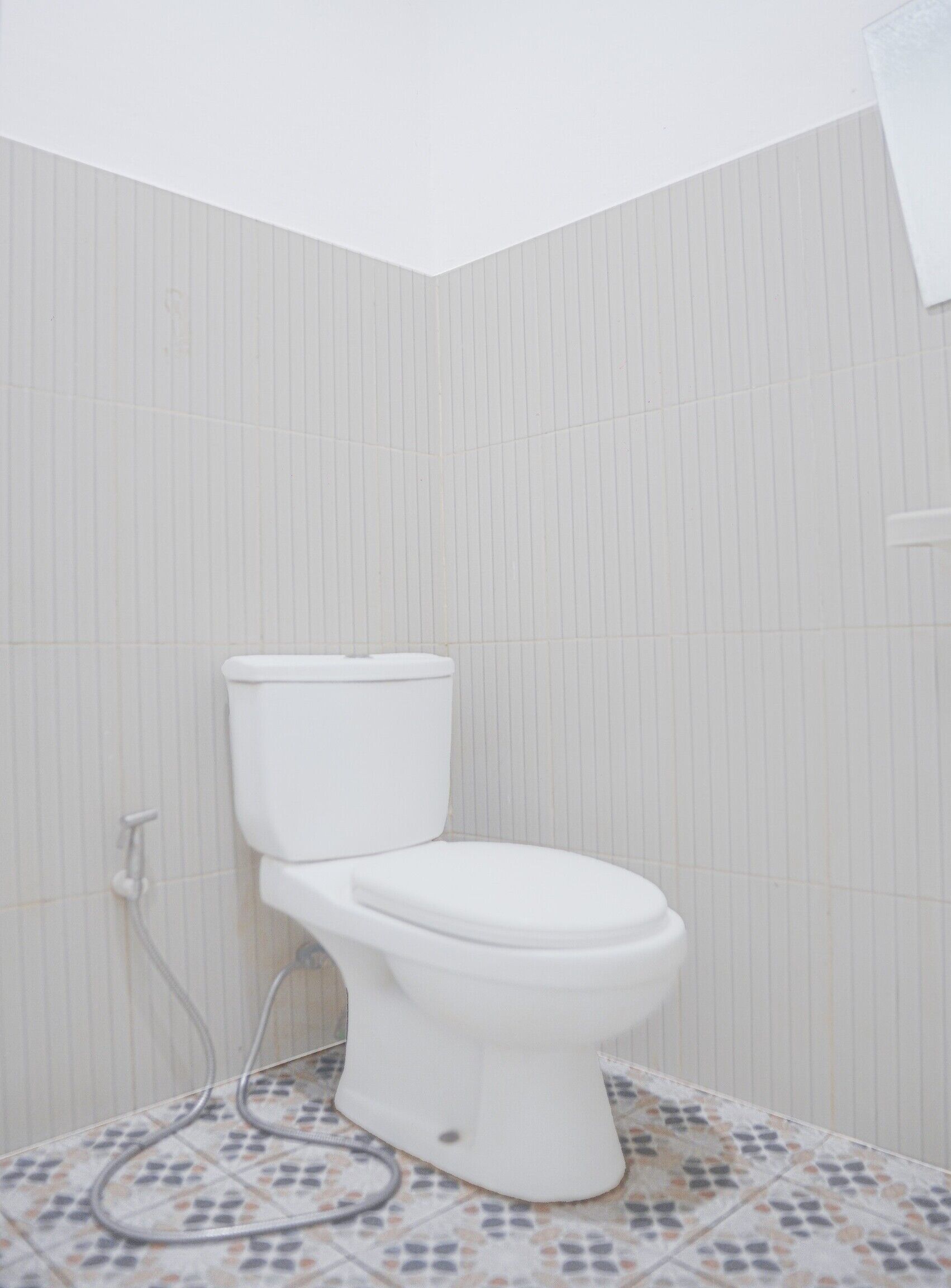 A white toilet in a bathroom with striped wallpaper and patterned floor tiles.