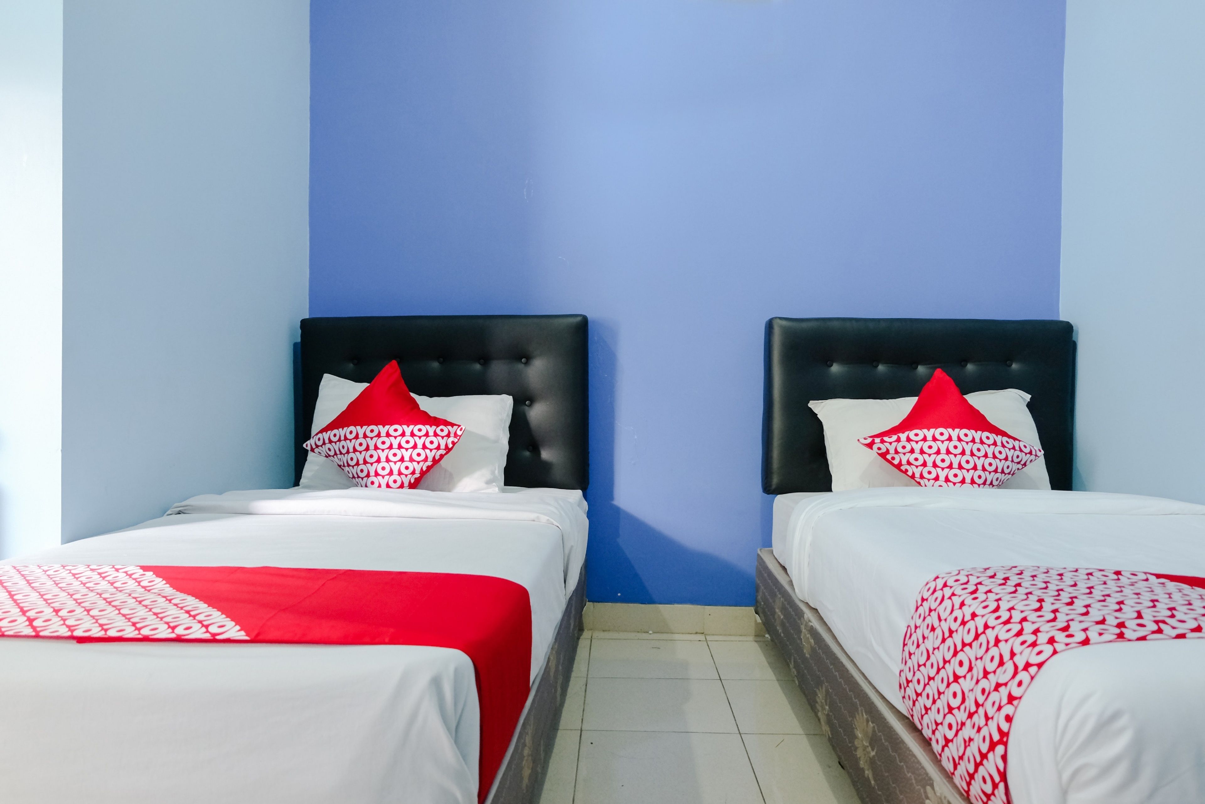 Dos camas individuales con cabeceros negros y ropa de cama con estampado rojo y blanco.