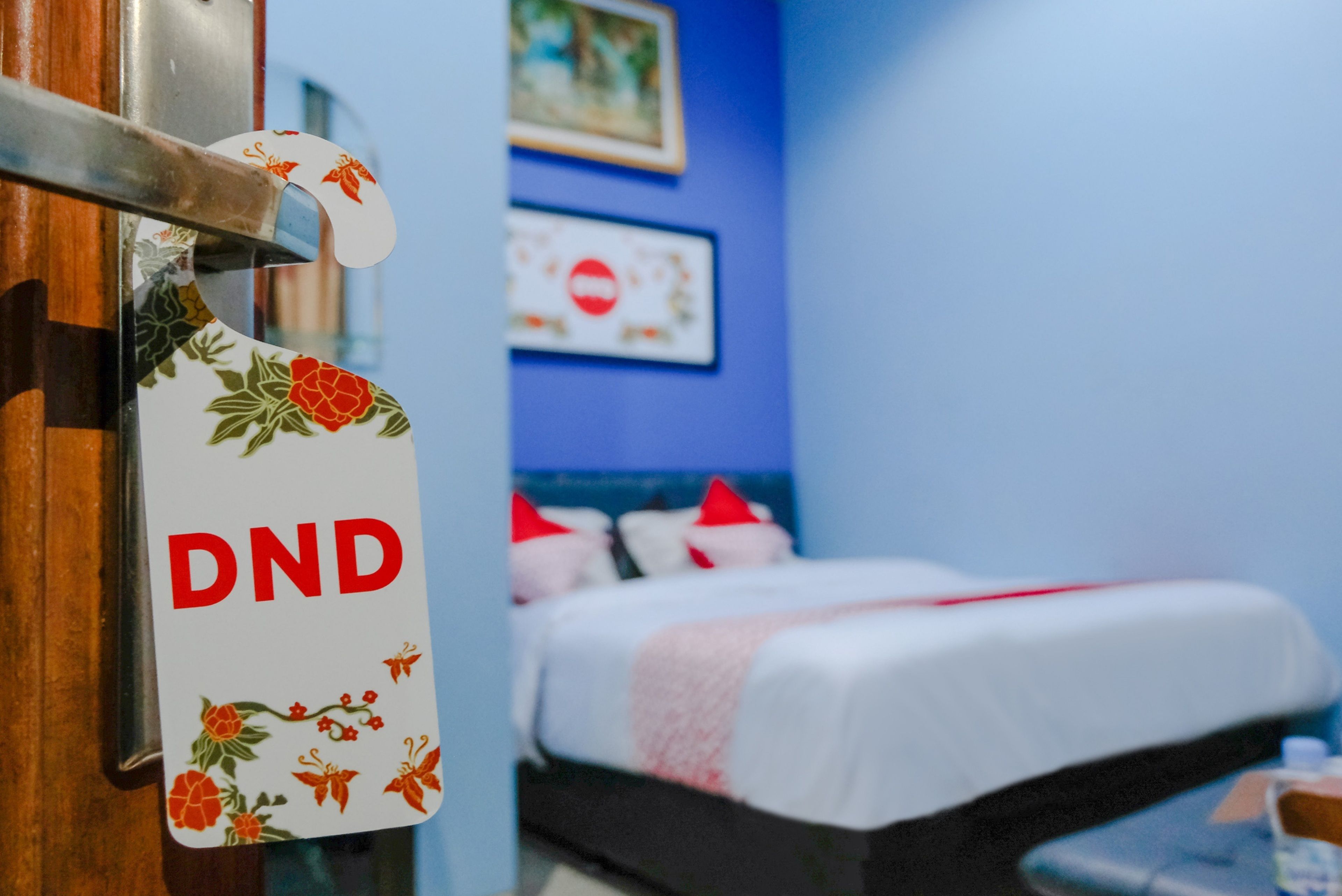 Ett hotellrum med en säng, en skylt med texten ”Stör ej” och en blå vägg med en tavla.