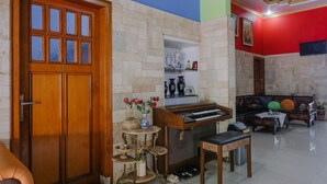 A room with a wooden door, a piano, a small table, and a sofa. - Hotel O Guest House Amalia Malang (Malang)