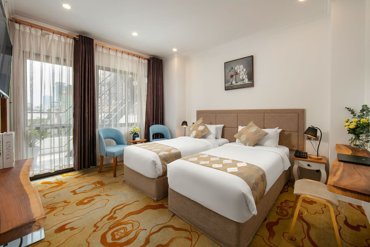 Een hotelkamer met twee bedden, een bureau, een stoel, een klein tafeltje en een raam met gordijnen.
