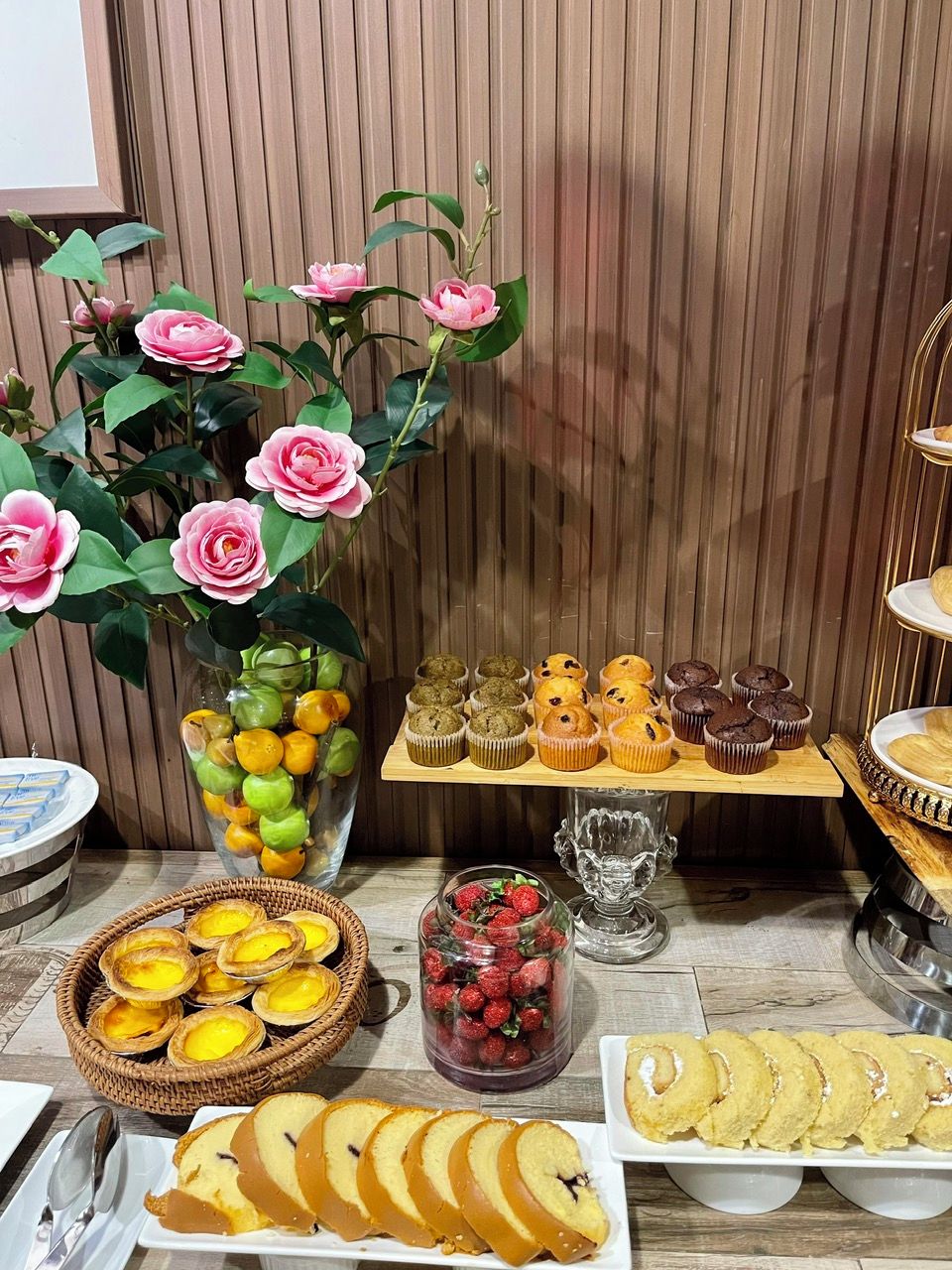 A table with various baked goods, including muffins and pastries, and a vase with artificial flowers.