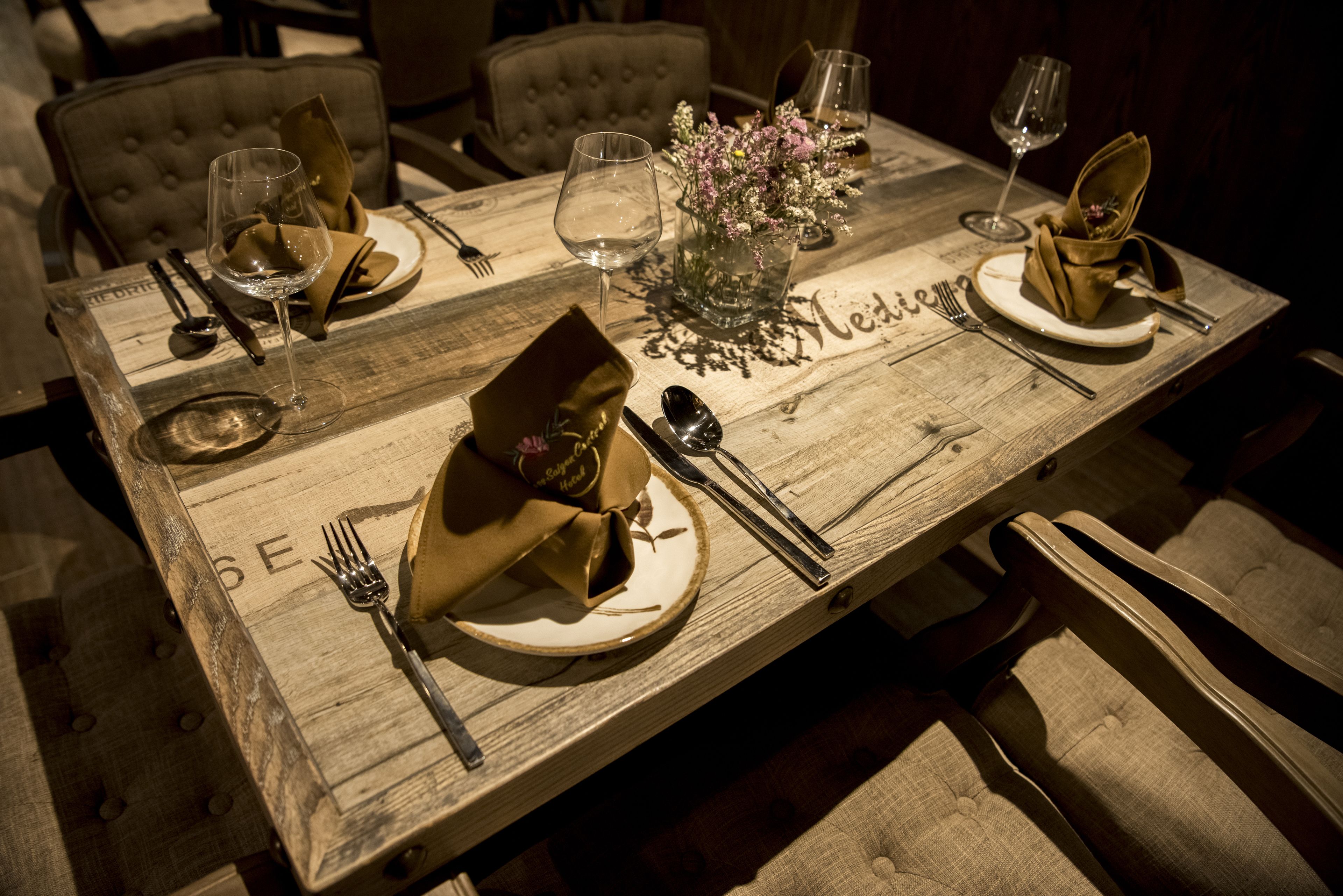 A wooden dining table set with plates, cutlery, and a vase with flowers.
