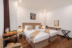 A hotel room with two beds, a small table with a tray of fruit and a glass of wine, a bedside table with a lamp, and a mirror on the wall. -  Nesta Hotel Saigon (Ho Chi Minh City)