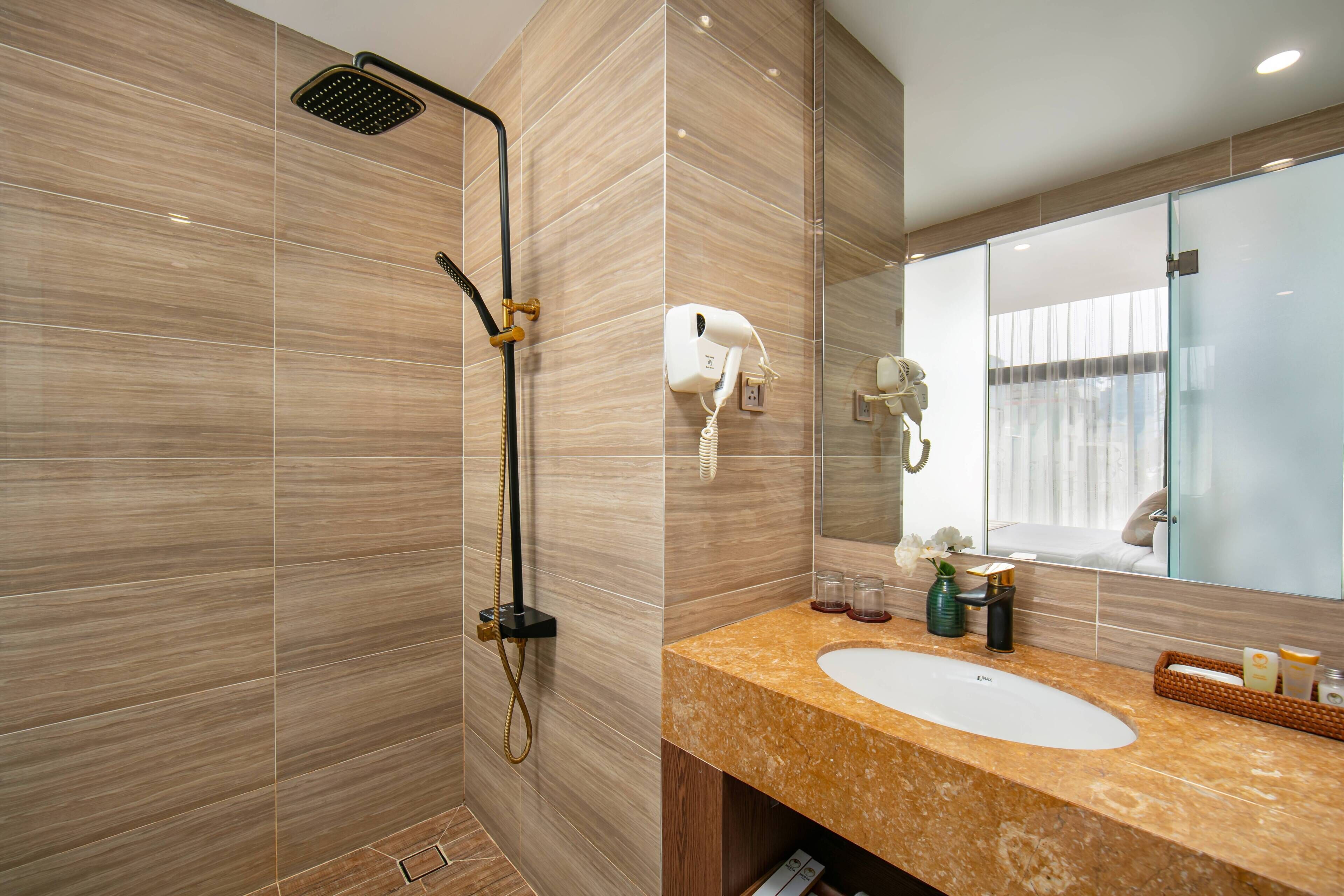 A bathroom with a shower, a sink, a hairdryer, and a mirror.