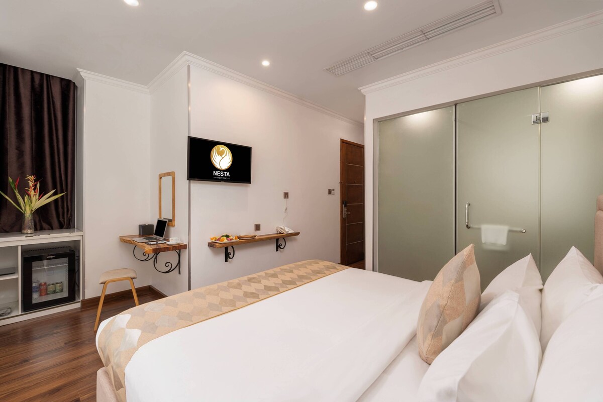 A hotel room with a bed, a desk with a laptop, a minibar, a mirror, and a wardrobe.