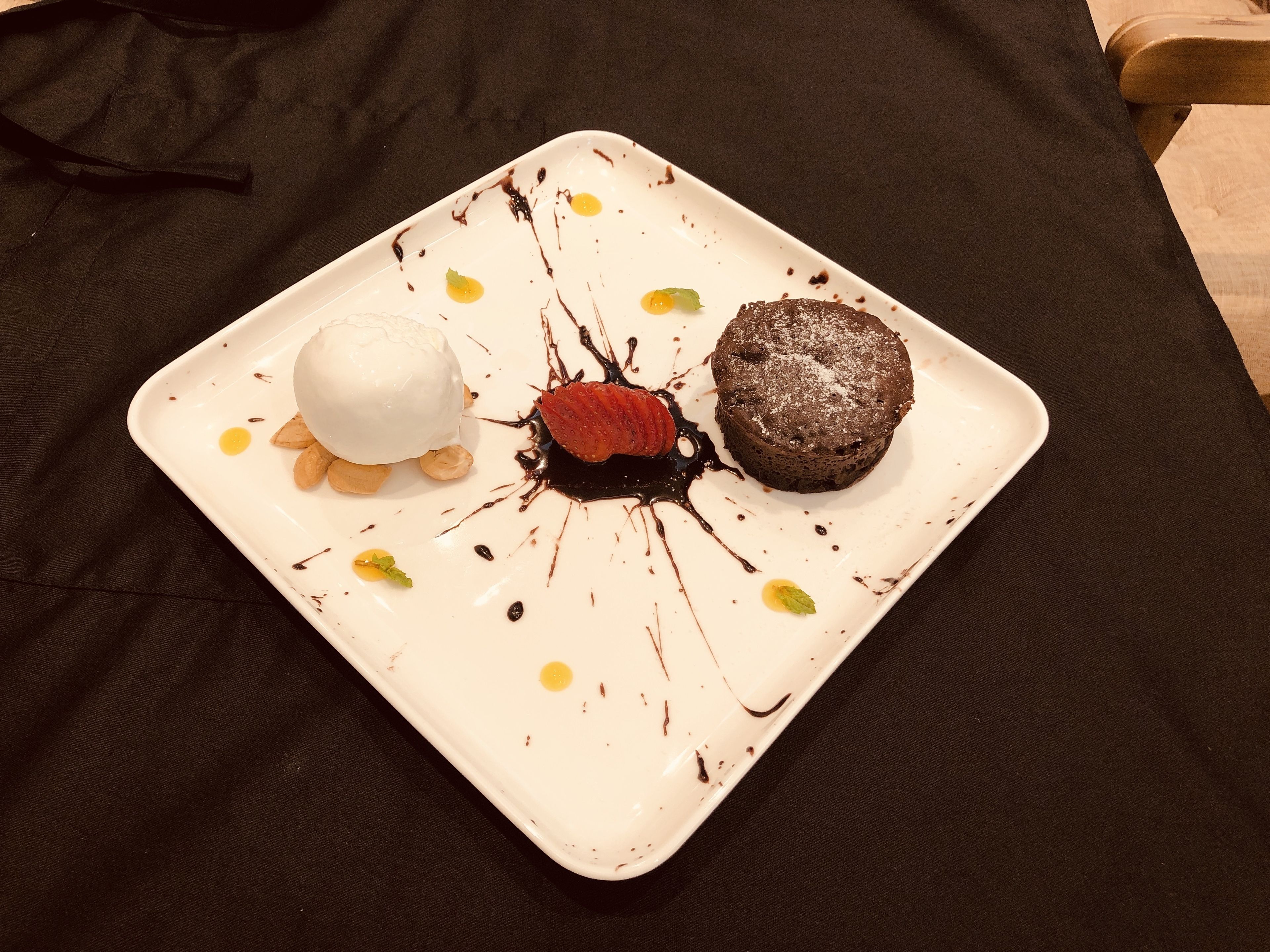 A dessert plate with a scoop of ice cream, a chocolate cake, and a strawberry on a white plate with chocolate drizzle.