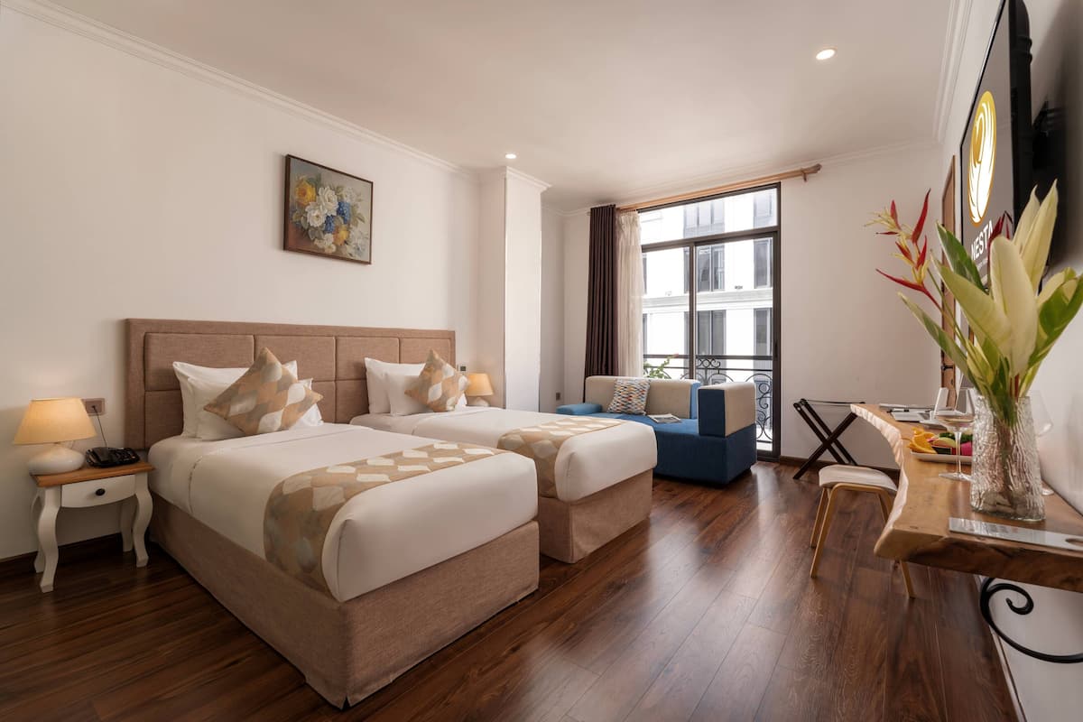 Een hotelkamer met een groot bed, een sofa, een bureau met een vaas en een raam met gordijnen.
