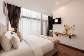 Een hotelkamer met een bed, een televisie, een plank met een vaas en een raam met gordijnen.