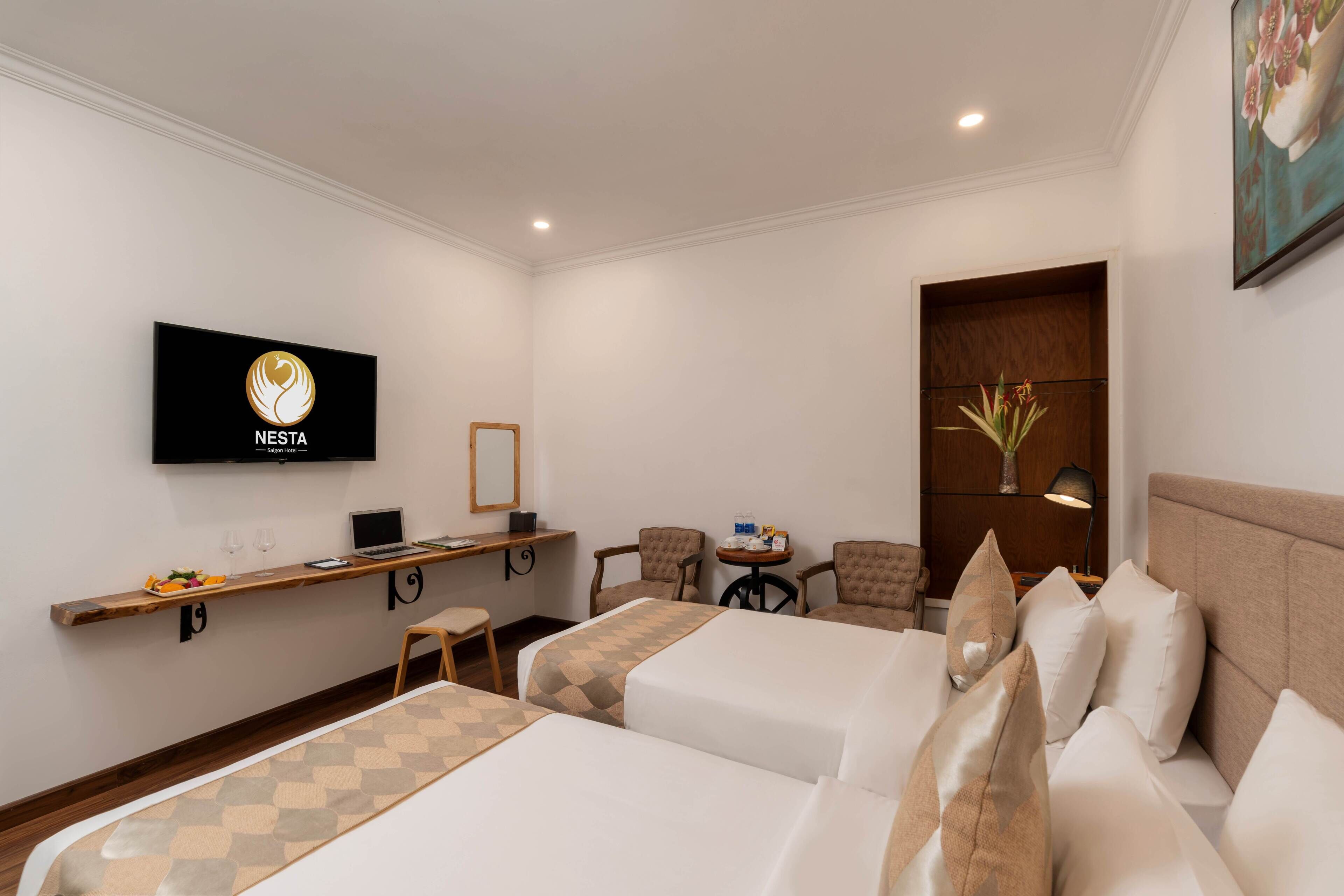 A hotel room with two beds, a TV, a desk with a laptop, a chair, and a small table with a vase.