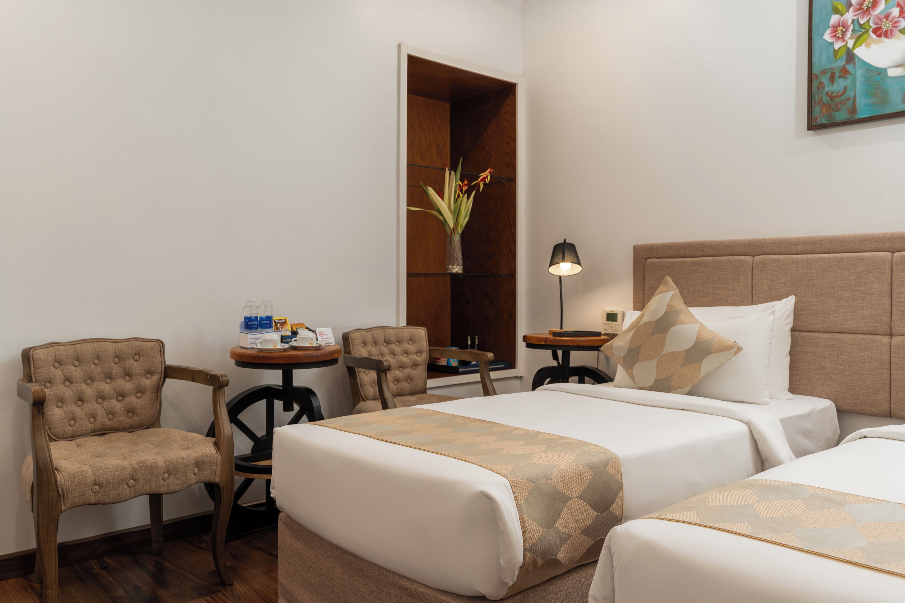 A hotel room with two beds, a sitting area with chairs, a small table, a lamp, and a painting on the wall.