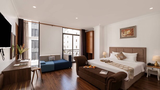 Een hotelkamer met een bed, een bureau, een bank, een stoel, een bijzettafeltje, een lamp en een schilderij aan de muur.