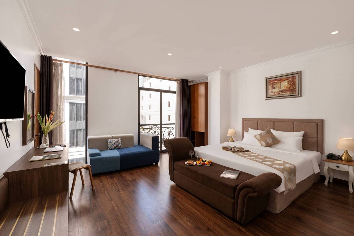 Een hotelkamer met een bed, een bureau, een bank, een stoel, een bijzettafeltje, een lamp en een schilderij aan de muur.