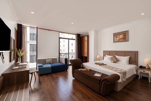 Een hotelkamer met een bed, een bureau, een bank, een stoel, een bijzettafeltje, een lamp en een schilderij aan de muur.