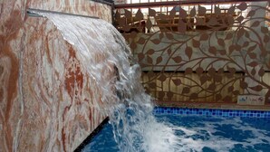 Een zwembad met een waterval en een decoratieve muur met bladmotieven.