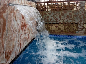 Een zwembad met een waterval en een decoratieve muur met bladmotieven.