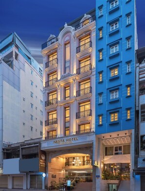 A multi-story hotel with a central entrance, balconies, and a sign indicating it is the NESTA HOTEL.
